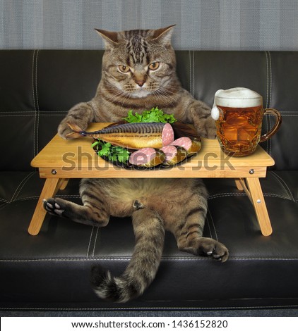 The cat is eating stuffed fish and drinking beer from the folding wooden bed tray on the sofa.