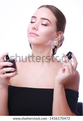 Fashion young makeup girl with closed eyes,wearing off shoulder black top,  long earrings,holding  a bottle of perfume and smelling aroma on the white background