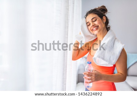 Woman drinking water at the home. Muscular woman taking break after exercise. Smiling attractive fitness woman with towel after training. Jogger run runner energy sweaty yoga vitality wellness concept Royalty-Free Stock Photo #1436224892