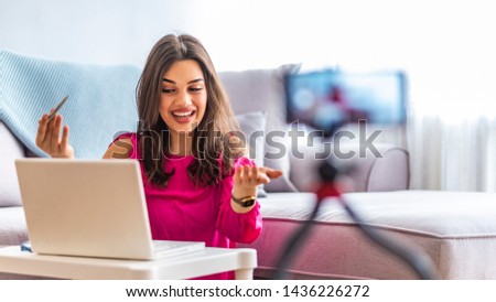 Happy girl at home speaking in front of camera for vlog. Young woman working as blogger, recording video tutorial for Internet. Young female blogger with laptop recording video at home

