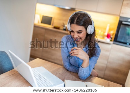 Portrait of a young executive girl watching video lecture on line sitting at home. Smiling businesswoman wearing headphones with laptop posing at workplace, happy woman in headset 
