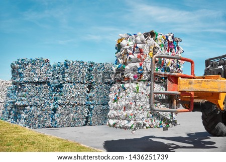 Loader holds big pressed plastic cubes of waste and rubbish at the plastic recycling plant near the big dump Royalty-Free Stock Photo #1436251739