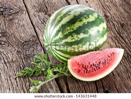 Watermelon with a slice and leaves on a wooden table.