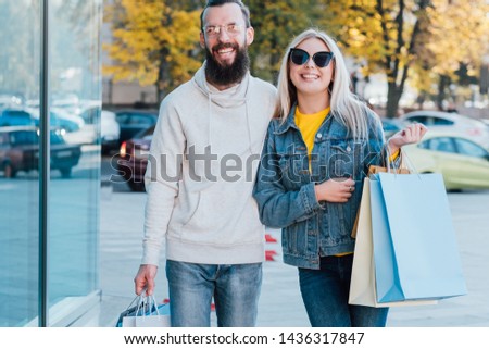 Shopaholics lifestyle. Happy couple standing with packages in city center. Blur fall landscape background.