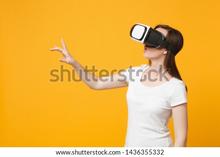 Young woman watching in headset of VR, touch something like push click on button pointing at floating virtual screen isolated on yellow orange background. People lifestyle concept. Mock up copy space