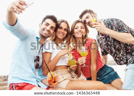 Group of young people taking a selfie with aperitif cocktails in hand against a white sky. Youth lifestyle leisure concept.