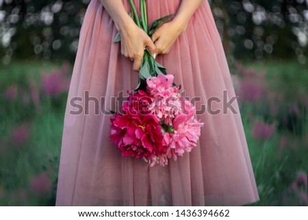 Romantic image of a woman in a pink tutu skirt holding a bunch of peonies in her hands in the natural flower bokeh background.