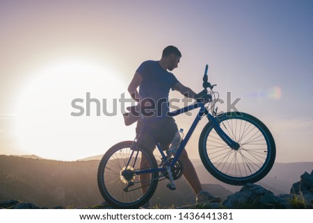 Mountain biker holding his bike on a rough cliff terrain on a sunset.