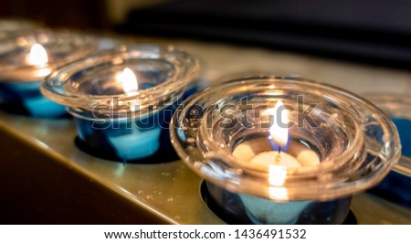 Close-up view of a series of devotional tea light candles arranged on a stand. Low-light image. Commonly seen inside churches.