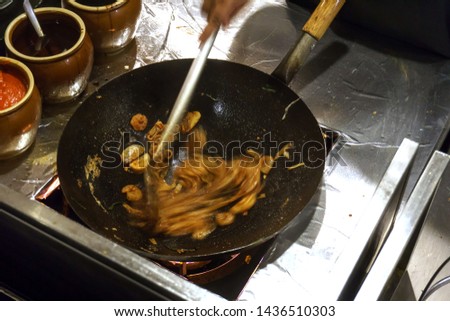 top down view of a short order cook vigorously stirring the Chinese style fried rice noodle dish, shot with slow shutter speed and resulting in blurred motion on the noodles and ladle.