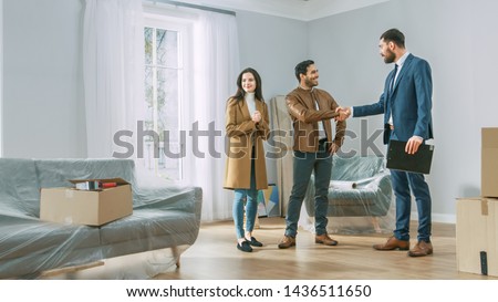 Professional Real Estate Agent Shows Bright New Apartment to Young Couple. Successful Young Couple Becoming Homeowners, Seal the Deal with Real Estate Broker by Handshake. Bright Home with Big Windows Royalty-Free Stock Photo #1436511650
