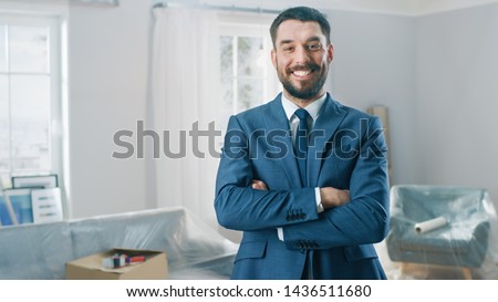 Successful Real Estate Agent in a Suit Smiles and Offers Keys From a New Apartment. Standing in the Middle of Room that Being Renovated. Spacious New House for Sale by Professional Real Estate Broker. Royalty-Free Stock Photo #1436511680