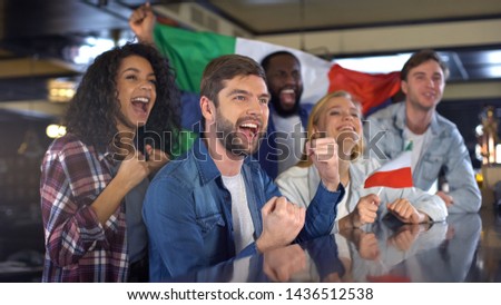 Cheerful Italian fans holding flag celebrating winning match, happy time in bar