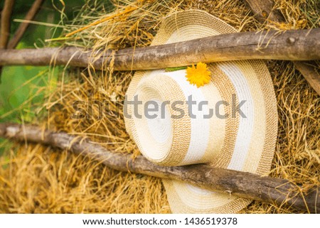 Rustic style, summer background screensavers. A straw hat with a flower hangs on the background of an old hayloft with dry grass. Panama under the wooden crossbar on the background of straw