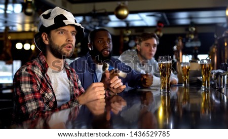 Anxious multiracial male friends watching match in bar, cheering for team goal