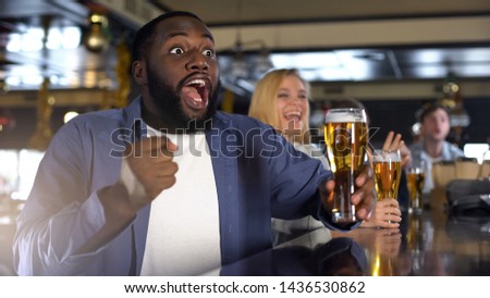 Extremely emotional black supporter watching game and holding beer glass, relax Royalty-Free Stock Photo #1436530862