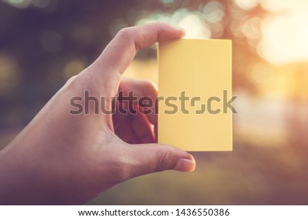 The hand is holding a color paper with empty space for note with a backdrop of sunlight and natural bokeh.