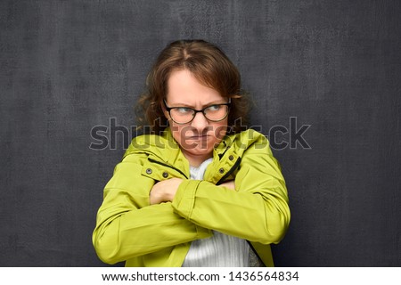 Studio portrait of discontented caucasian fair-haired young woman with glasses, frowning face, looking aside, holding arms crossed on chest with displeased and angry expression, over gray background Royalty-Free Stock Photo #1436564834