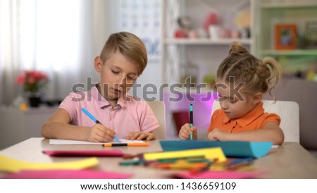 Adorable boy and girl drawing with pencils, sitting at table, kindergarten