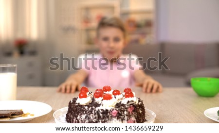 Excited little boy looking at delicious cake on kitchen table, sugar dessert