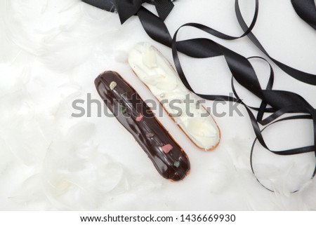 Set of two eclairs with a decor of black and white chocolate isolate on a white surface decorated with white feathers and brown ribbons, copyspace