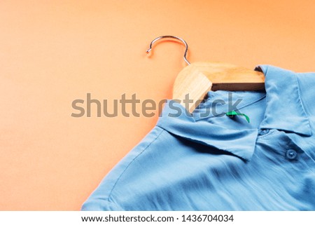 Blue woman's shirt on hanger on orange coral background.