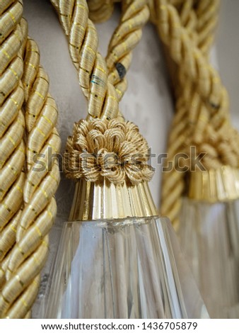 Decorative braided rope of gold color, tied into a knot. 
