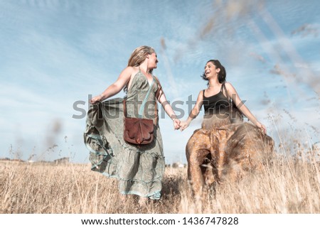 blonde and brunette girls smiling in the dry field in a sunset with dress and backpacks