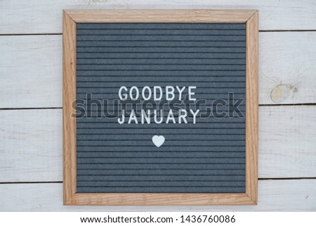 text in English goodbye January and a heart sign on a gray felt Board in a wooden frame. letter Board on white wooden background top view