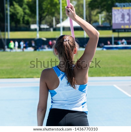 A high school girl holding a javelin overhead as she gets ready to compete in a track and field event.