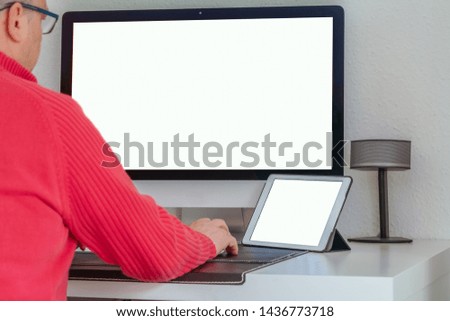 Old man working on tablet and computer at the desk. Tablet and computer screen mockup.