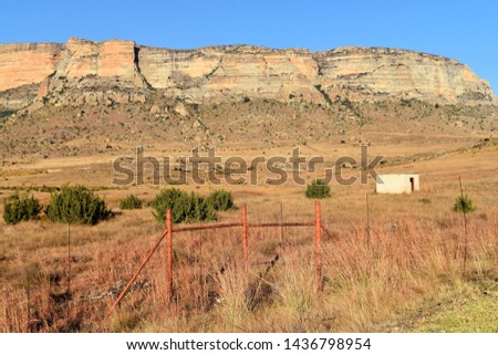 Landscape photo of Maluti mountains, Golden Gate Nature Reserve, South Africa, with farm fence and gate in the foreground and a deserted dwelling in the field