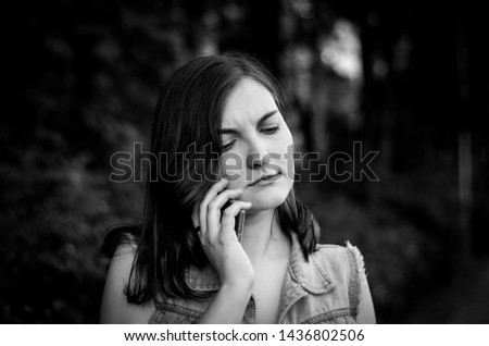 Girl talking on the phone and angry. Unpleasant conversation. Dissatisfaction. Spite. Brown hair with blue eyes. The glare of the sun. Photo. Black-white.