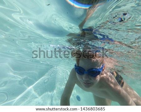 Little boys swimming and diving at pool under water shot. Underwater boy dived to bottom of pool. Little boy swims underwater in pool, smiling, blowing bubbles looking at me. Close-up. Horizontal