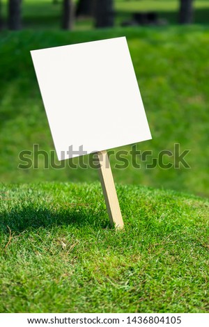 Empty white sign board on a small hill with freshly cut green grass and meadow in the background