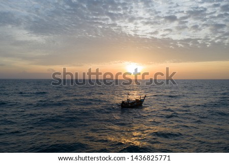 Aerial drone view of sea with drifting fishing boat over amazing sunset with cloudy sky