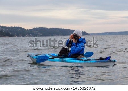 Adventure photographer taking pictures with his camera from a kayak in the ocean. Taken in Howe Sound near Horseshoe Bay, West Vancouver, British Columbia, Canada.