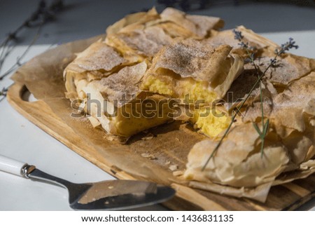 Pieces of homemade traditional Greek pastry -- bougatsa made of phyllo dough and semolina custard iced with sugar and cinnamon powder on wooden board.