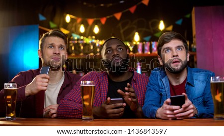 Multiethnic male friends watching football match in pub, upset with team losing