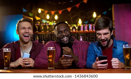 Happy multiethnic friends celebrating team victory, checking results online Royalty-Free Stock Photo #1436843600