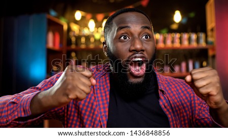 Extremely happy african-american fan celebrating favorite team victory in pub