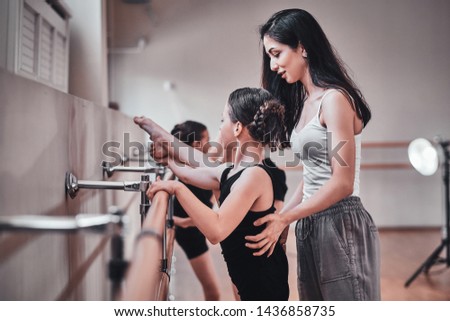 Young pensive girl got special ballet rehearsal from cheerful dilligent trainer at bright training room.