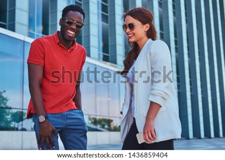 Happy smiling bisness partners in sunglasses meeteng up near glass building at city centre.