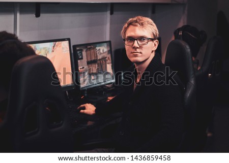 Pensive young gamer in glasses is playing videogames at popular cyber club.