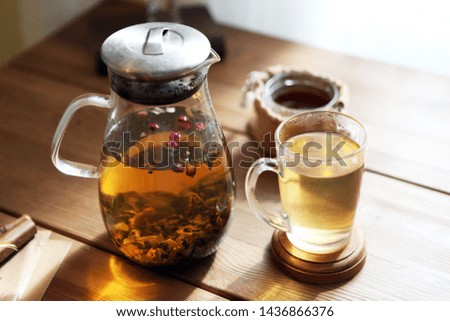 Traditional herbal tea with glass teapot, cup, dried roses buds with honey on wooden table at home, sunlight background, selective focus, copy space