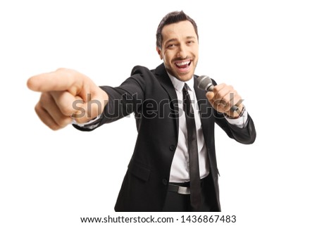 Cheerful man in a suit pointing towards the camera and holding a microphone isolated on white backround