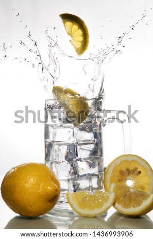 Lemons falling into a glass of ice water with splashes against isolated on white background. Refreshing Beverage