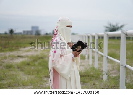Beautiful asian Young muslim woman use niqab reading book Quran  in the park outdoors