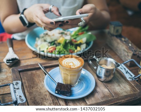 Woman's hands taking photo of coffee cup, Piccolo Latte, brownies with breakfast on wooden table by smartphone.