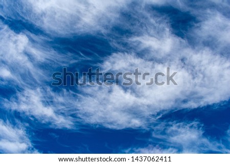 Wispy white clouds blow over a dark blue sky offering a natural and organic background. 